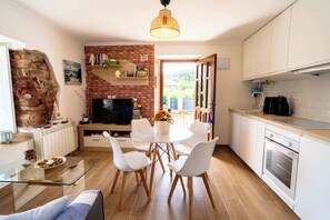 Una cocina moderna con armarios blancos, una chimenea de ladrillo y un comedor con sillas blancas.