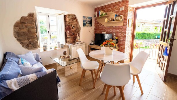 A living room with a sofa, a dining table with chairs, a TV, and a brick wall.