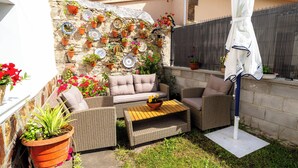 A patio with wicker furniture, a stone wall with potted plants, and a white umbrella.