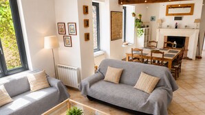 A living room with two grey sofas, a coffee table with a book, a fireplace, and a dining area with wooden furniture. - Charming country house in a flower garden between Paris and Chartres (Yermenonville)