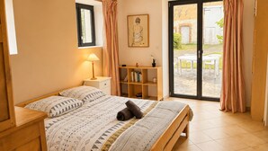 A bedroom with a bed, a nightstand, a bookshelf, and a sliding glass door to an outdoor patio. - Charming country house in a flower garden between Paris and Chartres (Yermenonville)