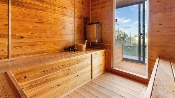 A wooden cabin interior with a wooden bench, a metal bucket, and a window. - The Padel Villa (Pinos de Alhaurín)