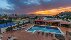 A rooftop pool area with lounge chairs, a swimming pool, and a view of the sunset over mountains. - The Padel Villa (Pinos de Alhaurín)