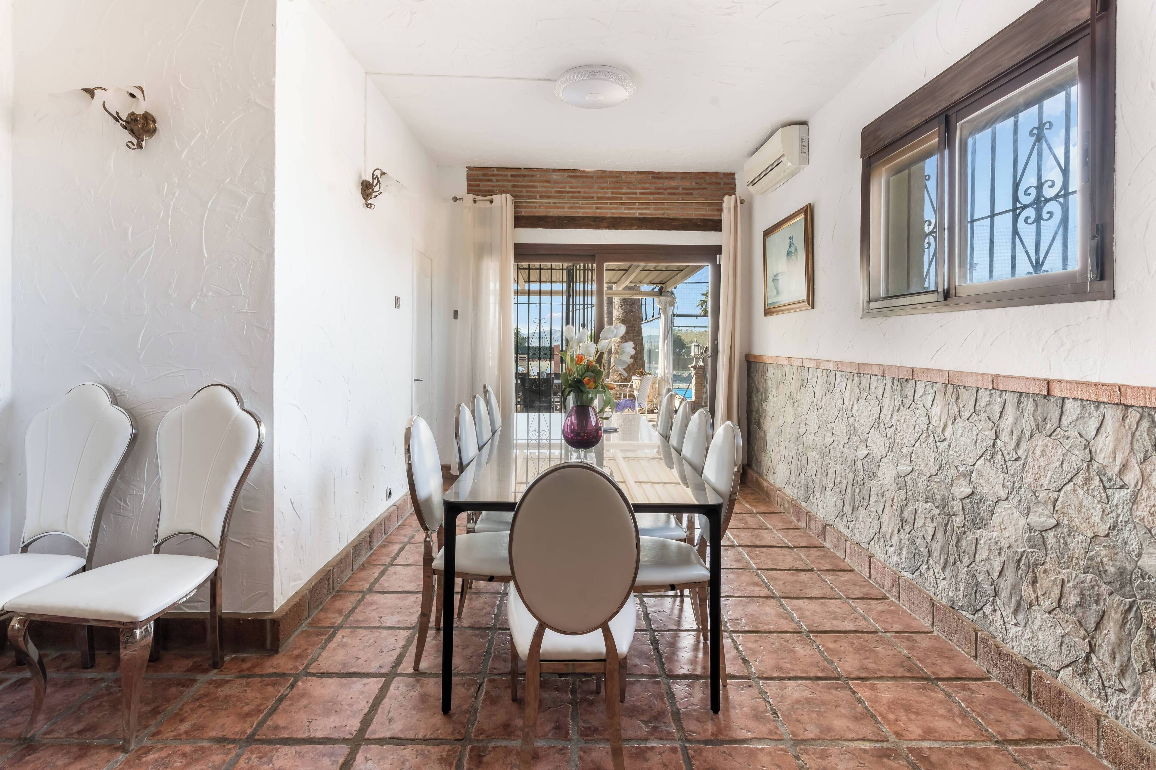 A dining area with a long table, chairs, and a view through an open door.