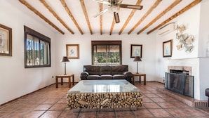 A living room with a fireplace, a sofa, a coffee table, and a ceiling fan. - The Padel Villa (Pinos de Alhaurín)
