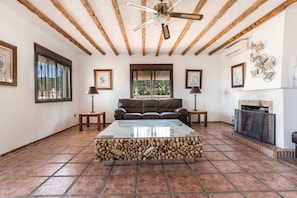 A living room with a fireplace, a sofa, a coffee table, and a ceiling fan. - The Padel Villa (Pinos de Alhaurín)