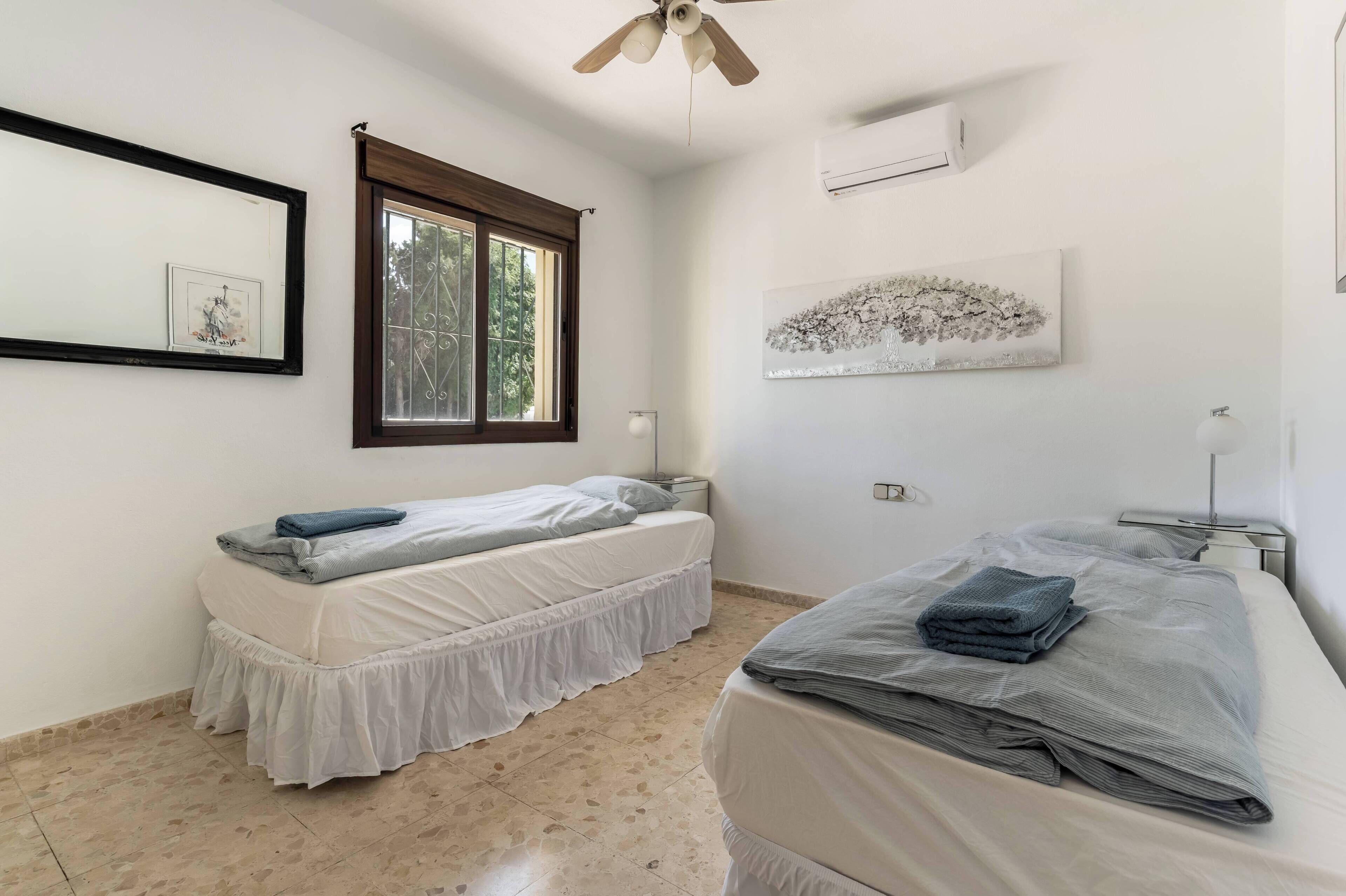 A bedroom with two beds, a window, an air conditioner, and a ceiling fan.