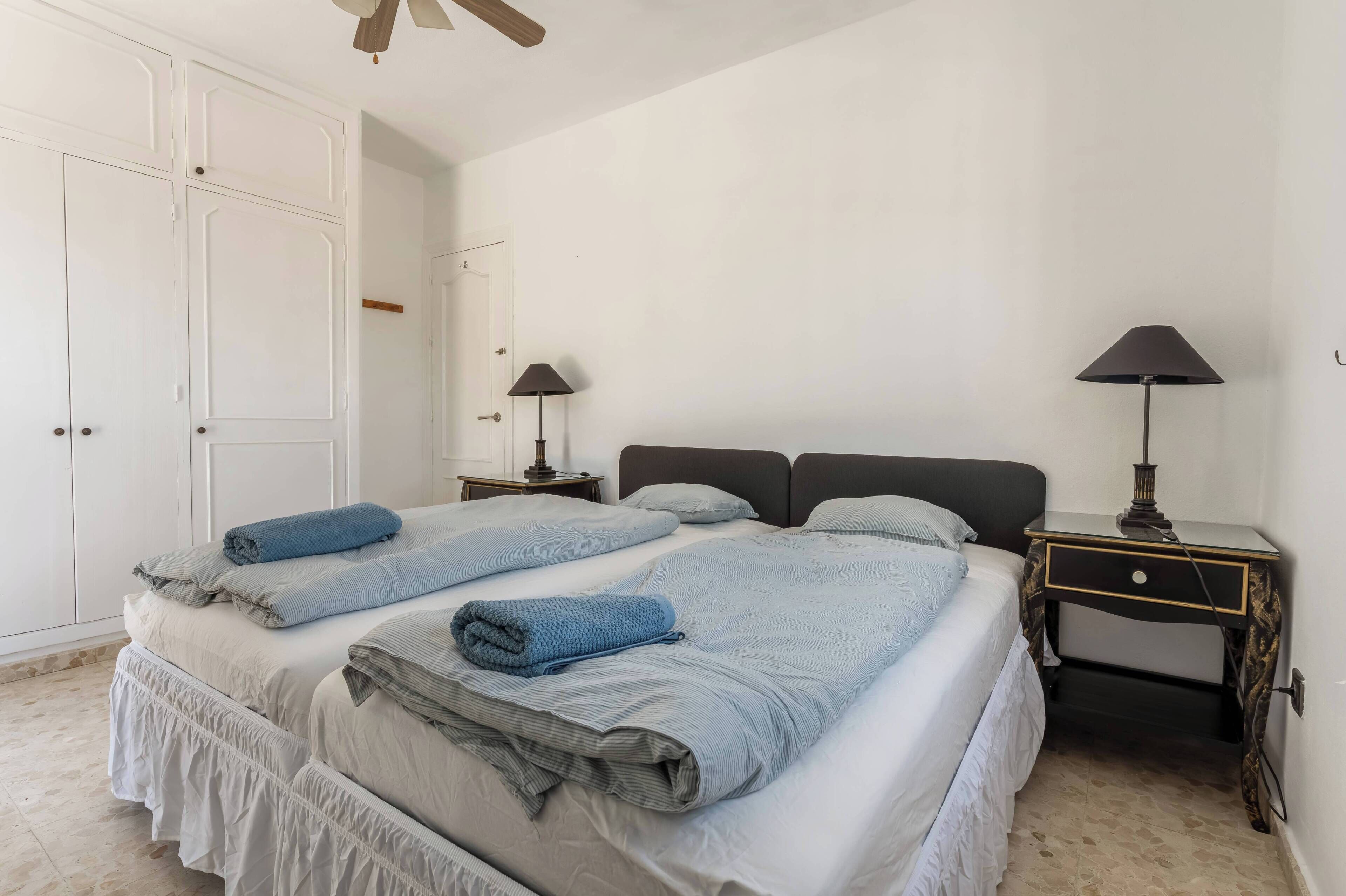 A bedroom with two beds, a wardrobe, bedside tables, and lamps.