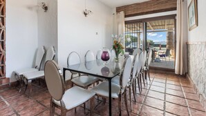 A dining area with a glass table and chairs, a vase with flowers, and a view through a glass door. - The Padel Villa (Pinos de Alhaurín)