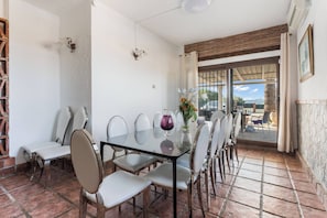 A dining area with a glass table and chairs, a vase with flowers, and a view through a glass door. - The Padel Villa (Pinos de Alhaurín)