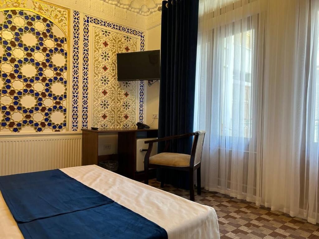 Une chambre d’hôtel avec un lit, un bureau, une chaise, une télévision et une fenêtre avec des rideaux.