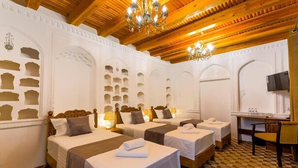 Une chambre d’hôtel avec quatre lits, un bureau, une chaise et un lustre.