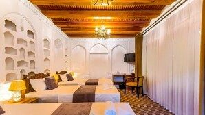 Une chambre d’hôtel avec trois lits, un lustre, une télévision et un sol à carreaux.