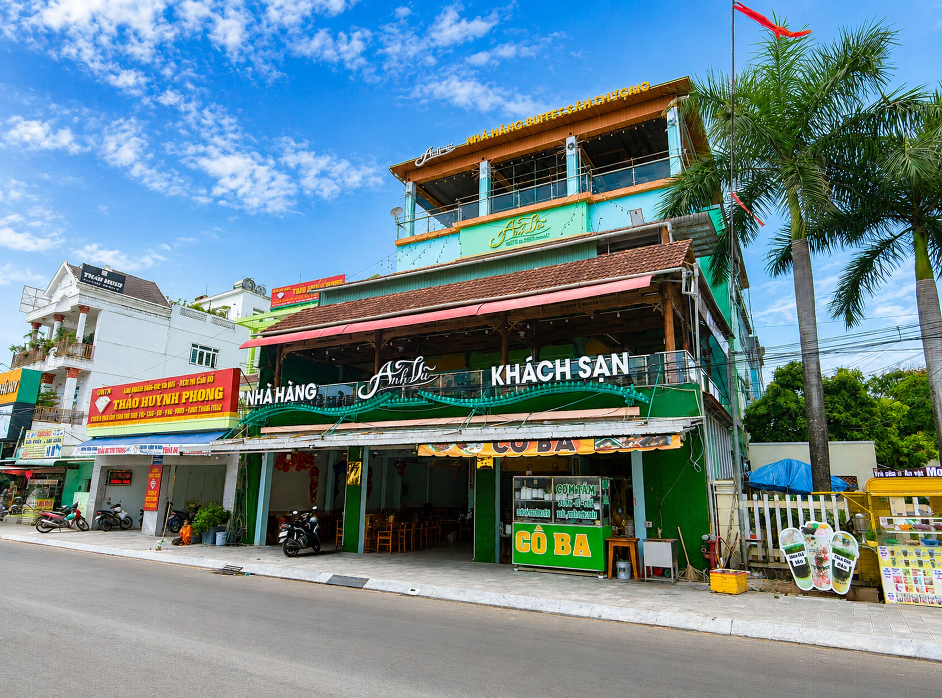 A multi-story building with a green facade, a sign reading 'KHACH SAN,' and a small outdoor seating area.