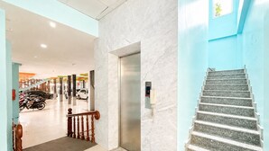 Un vestíbulo de hotel con una pared de mármol, un ascensor, una escalera y coches estacionados.