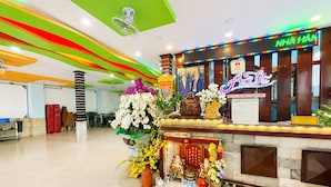Zona de recepción de hotel con un letrero de neón, un mostrador de recepción y un altar decorativo con ofrendas.