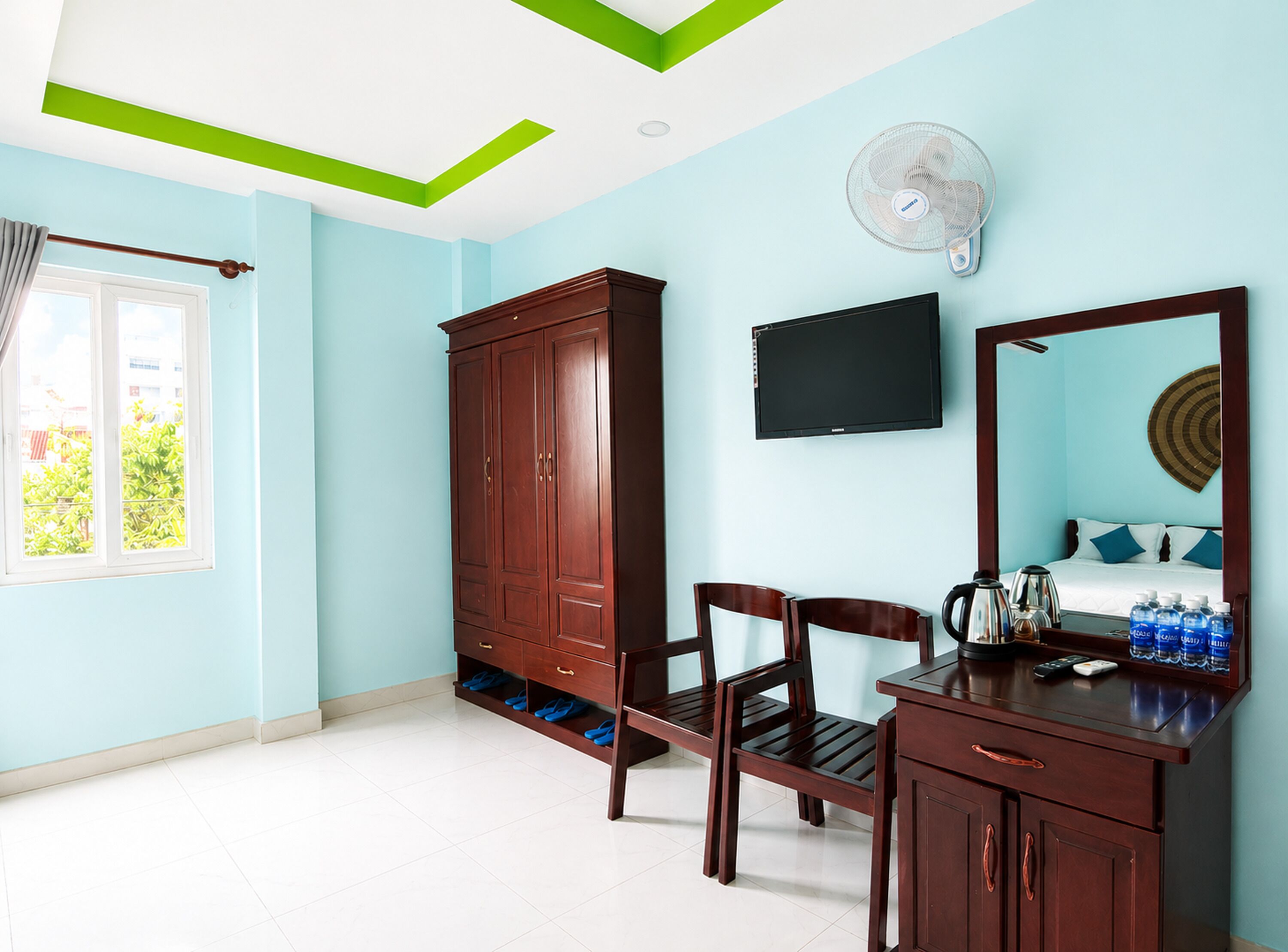 A room with a wardrobe, a desk with a mirror, a television, and a fan.