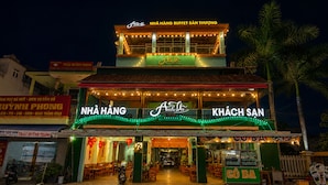 Un restaurante con terraza, un letrero que dice 'NHÀ HÀNG' y 'KHÁCH SAN', y un letrero de neón sobre la entrada.