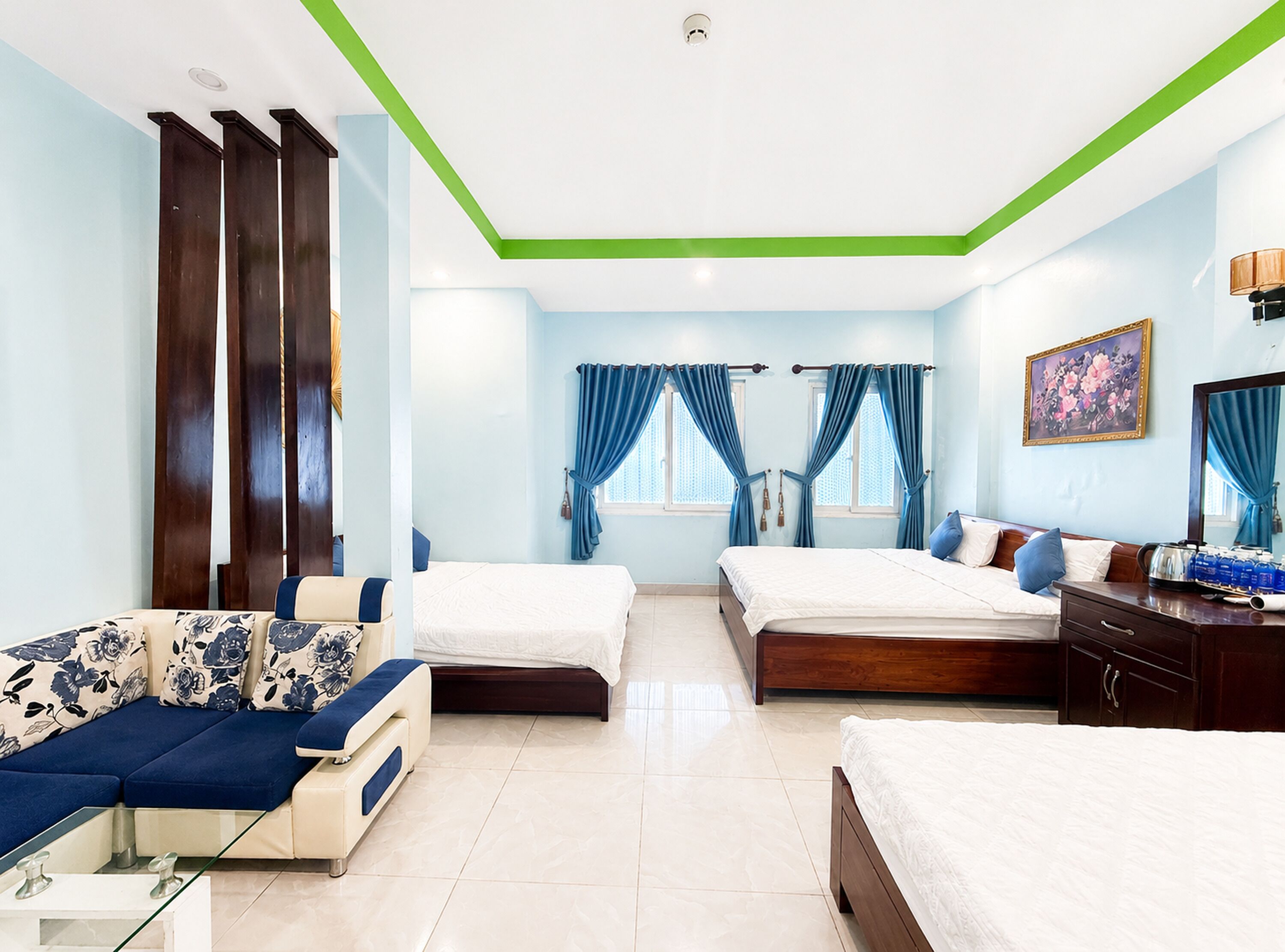 A hotel room with two beds, a sofa, a desk, and a painting on the wall.