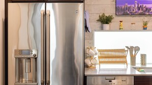 Een roestvrijstalen koelkast met een waterdispenser, een vaatwasser en een stadsgezichtschilderij aan de muur.