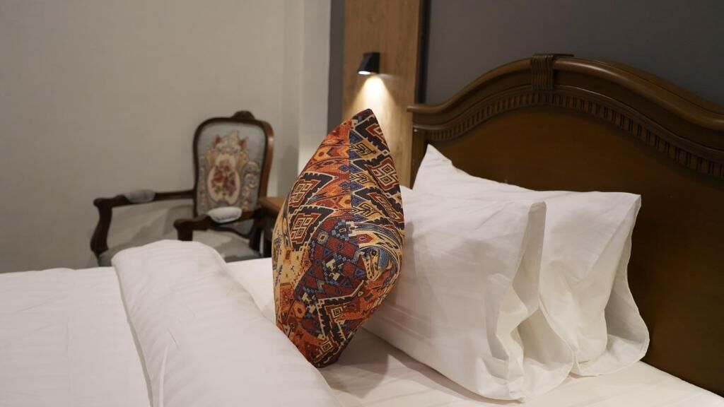 A bed with white linens, a patterned pillow, and a wooden headboard.