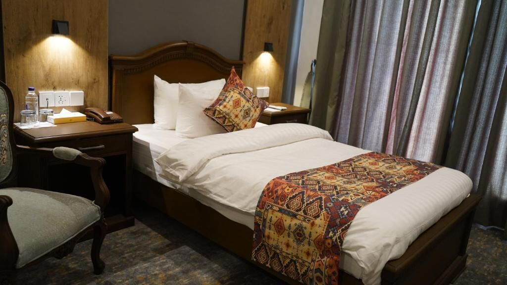 A hotel room with a bed, a desk, a chair, and a nightstand.