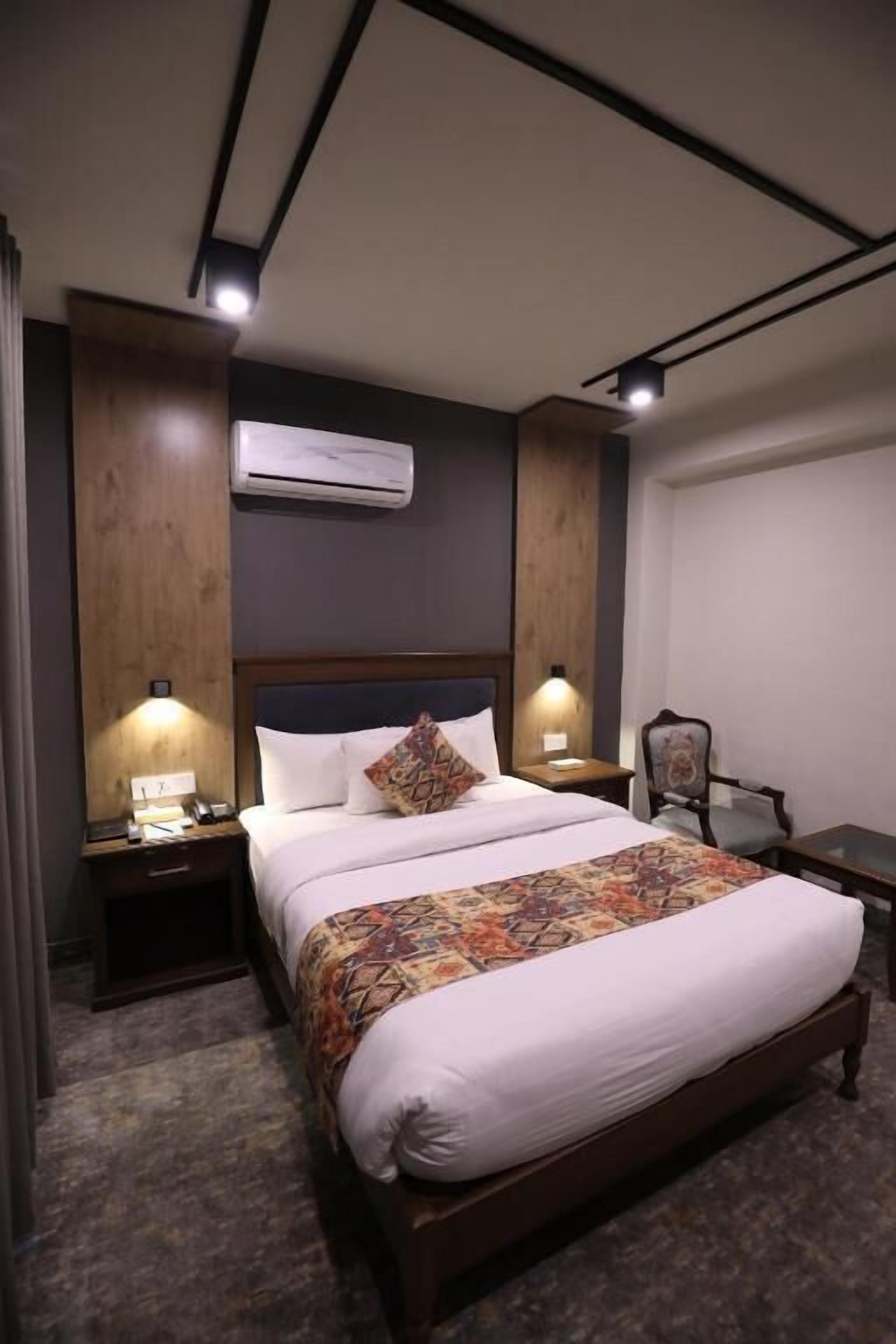 A hotel room with a bed, bedside tables, an air conditioning unit, and a chair.