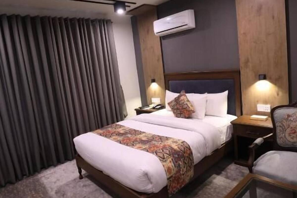 Habitación de hotel con cama, mesitas de noche, una silla, un escritorio, aire acondicionado y cortinas.