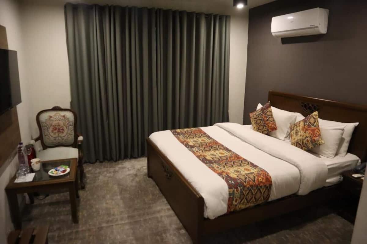 Habitación de hotel con cama, una silla, una mesita y aire acondicionado instalado en la pared.