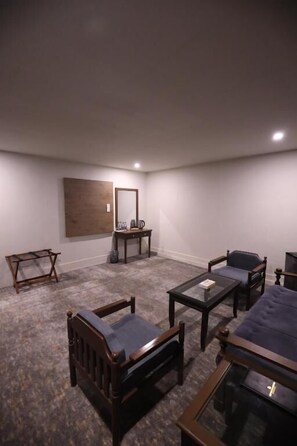 A room with a carpeted floor, a wooden chair, a small table, a larger table, a sofa, and a mirror on the wall.