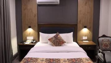 A hotel room with a large bed, two bedside tables, an air conditioning unit, and a chair.