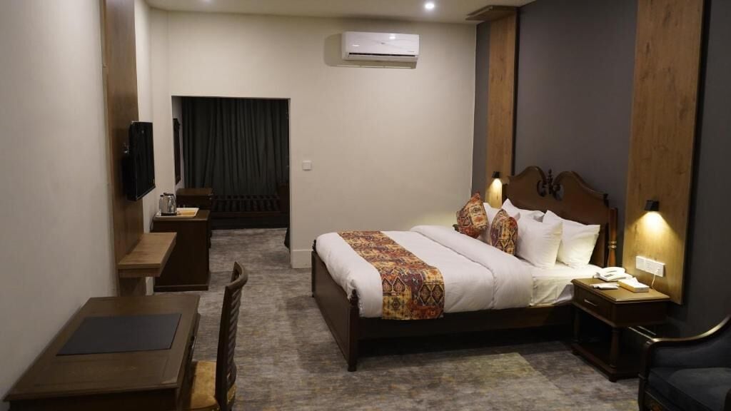 A hotel room with a bed, bedside table, lamp, and a television on a stand.