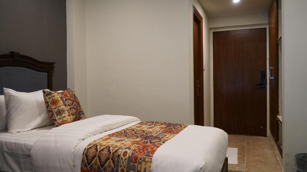 A bedroom with a bed, pillows, a patterned blanket, a wooden door, and a tiled floor.