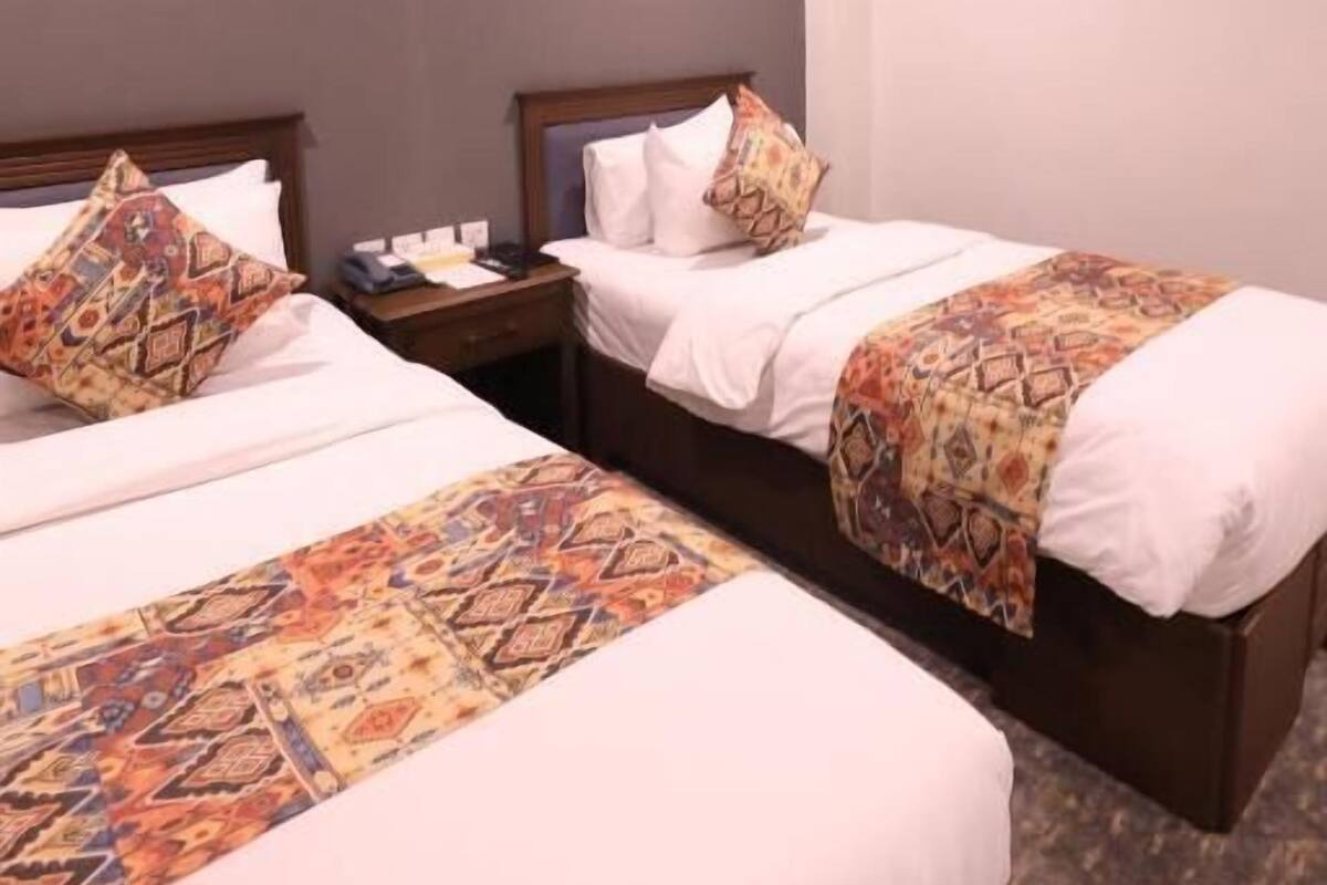 Una habitación de hotel con dos camas, una mesita de noche, aire acondicionado e iluminación en el techo.