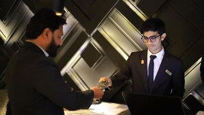 En man i kostym räcker över ett visitkort till en annan man vid receptionsdisken i en modern hotellobby.