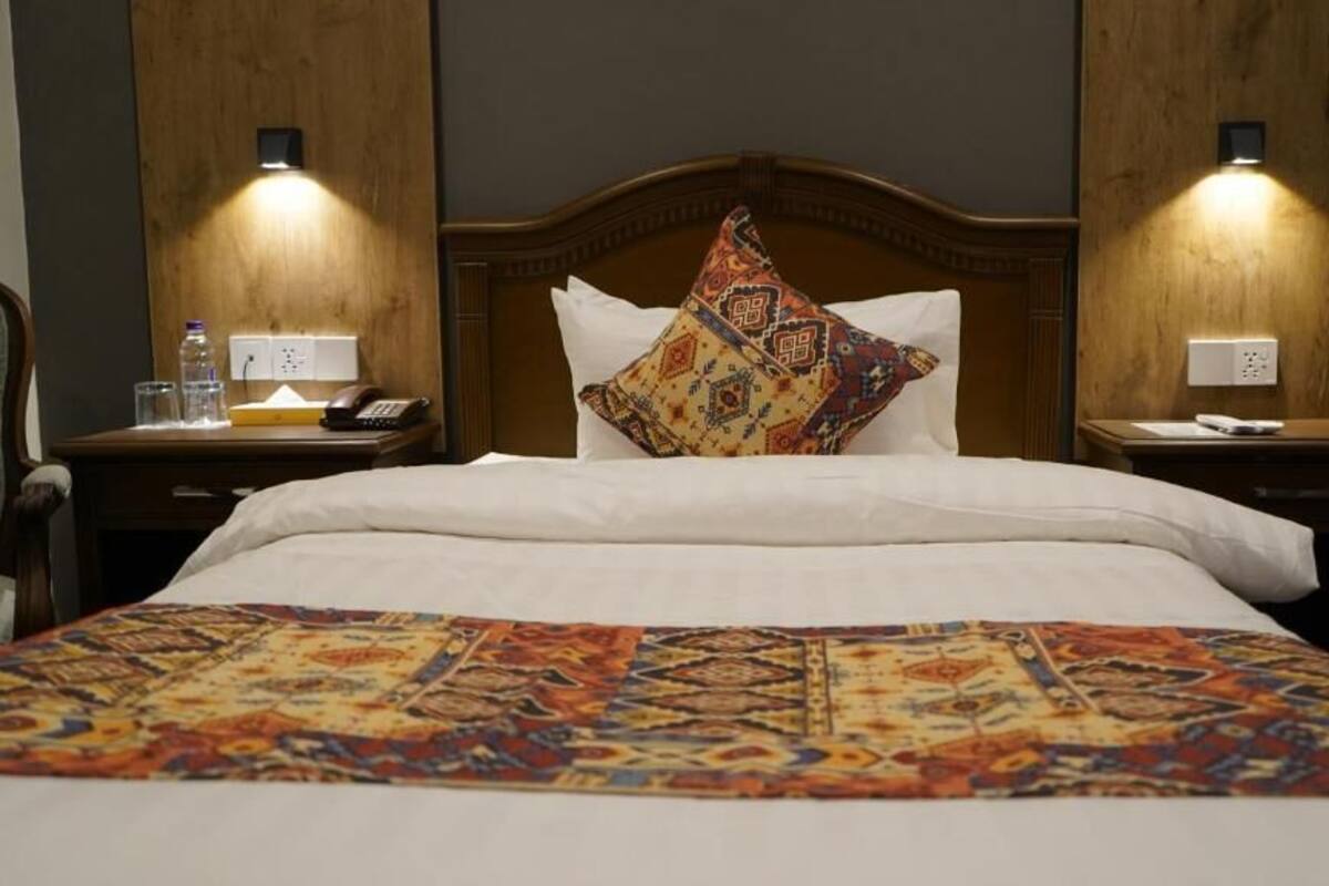 Habitación de hotel con cabecera de madera, colcha estampada, dos mesitas de noche con lámparas y una mesita auxiliar con teléfono y lámpara.