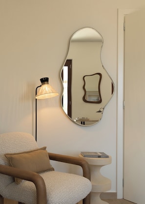 Una habitación con una silla, una lámpara, un espejo y una mesita.
