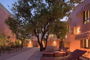 A courtyard with a tree, lounge chairs, and a stone fireplace.