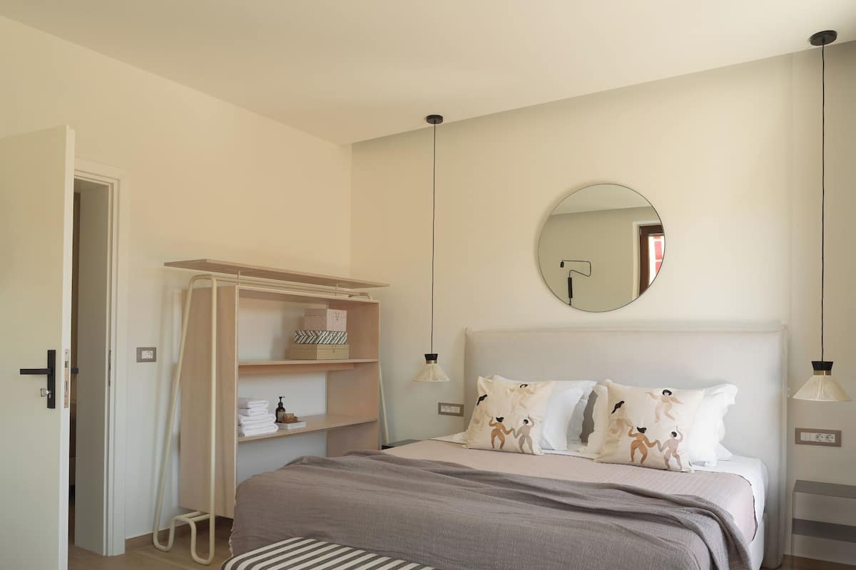 A bedroom with a bed, a bedside table, a mirror, a wardrobe, and a bench.