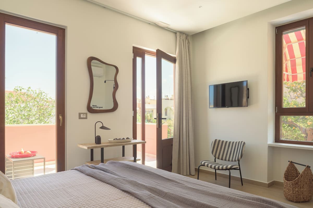 Quarto com cama, escrivaninha, cadeira, televisão e porta para varanda.