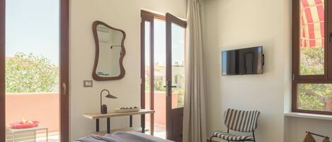 A bedroom with a bed, a desk, a chair, a TV, and a balcony door.