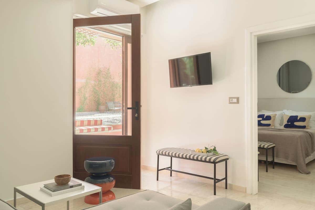 Quarto de hotel moderno com cama, televisão, um banco e uma pequena mesa com livros.