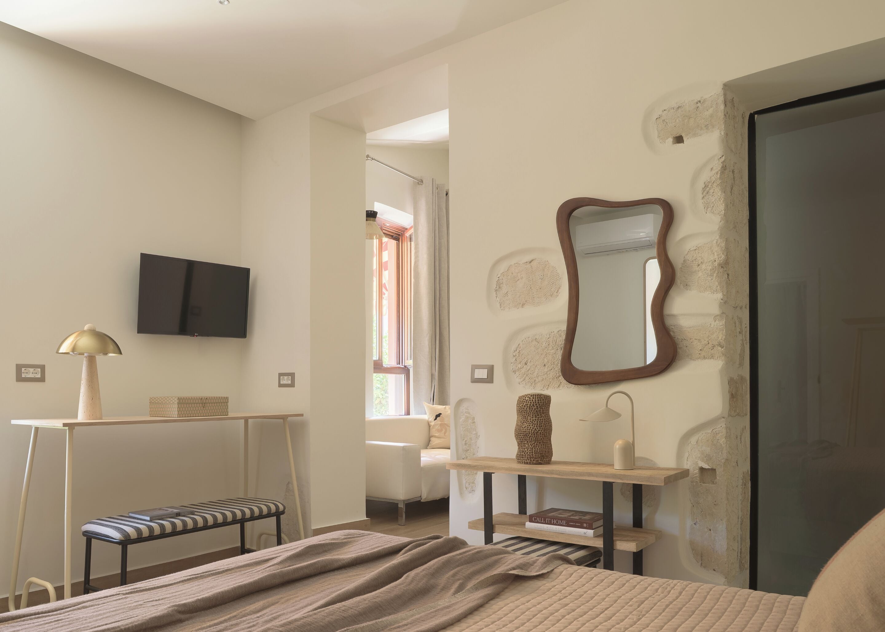 Un dormitorio con cama, mesita de noche, lámpara, silla y televisor montado en la pared.