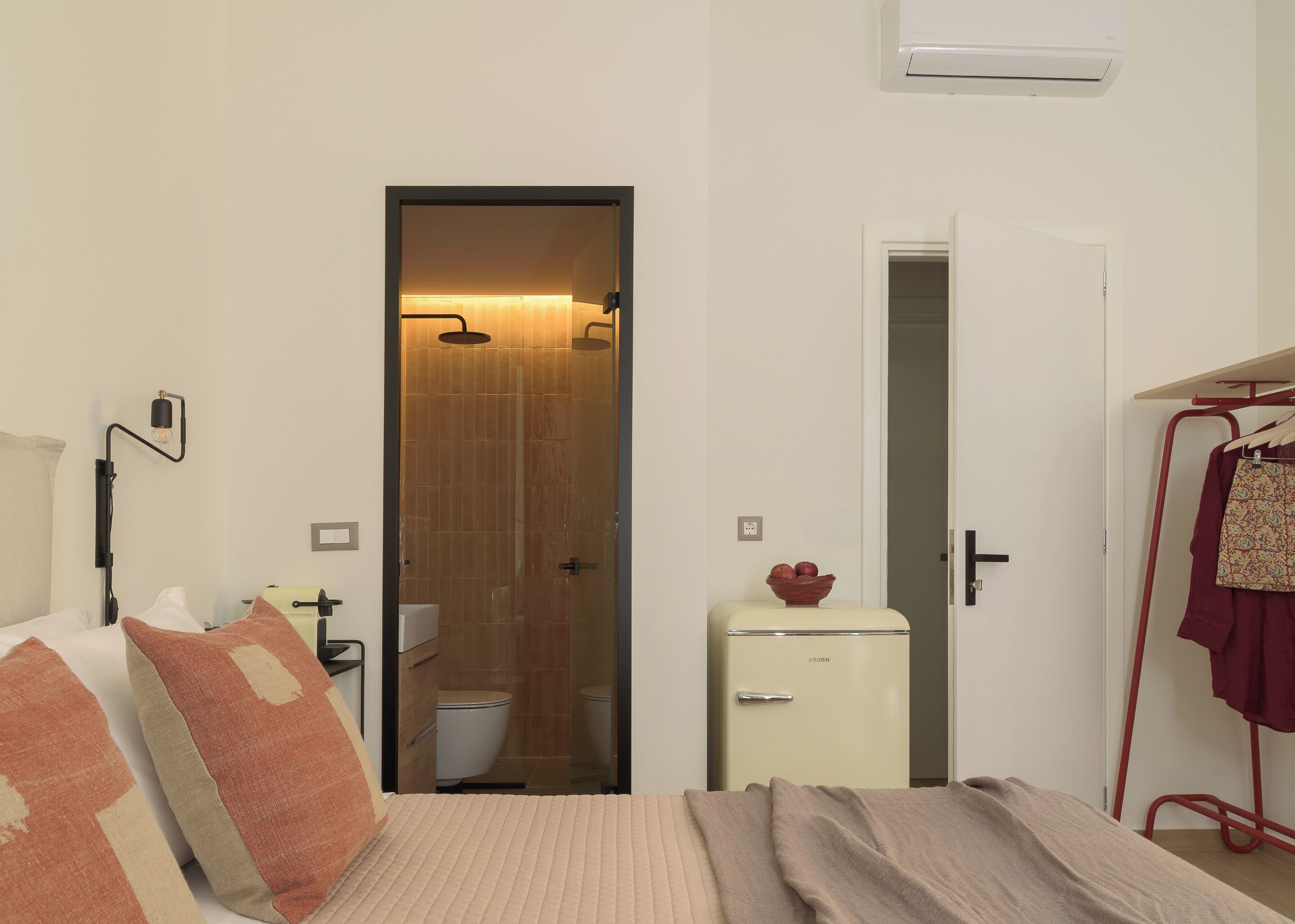 Une chambre à coucher comprenant un lit, une table de chevet, une armoire, un petit meuble et une salle de bain visible à travers une porte ouverte.