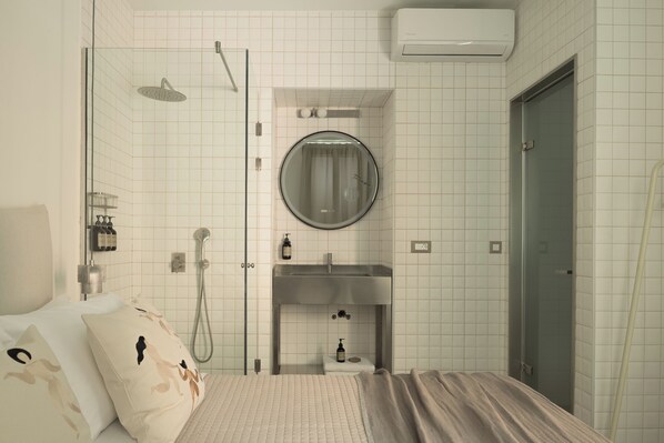 A hotel room with a bed, a shower, a sink, and a mirror.