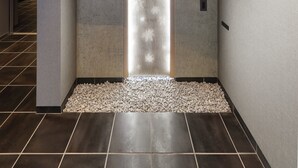 A modern interior with a wooden beam ceiling, a stone wall with a light feature, and a tiled floor. - HAKU HIROSHIMA Station HOTEL (Hiroshima)