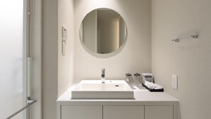 A modern bathroom with a white vanity, a round mirror, and a shower area. - HAKU HIROSHIMA Station HOTEL (Hiroshima)
