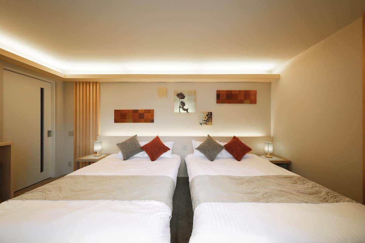 Una habitación de hotel con dos camas, una mesita de noche con lámpara, una obra de arte en la pared y una puerta.