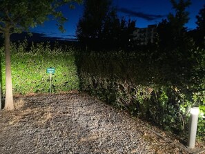 A gravel pathway leading to a parking area, surrounded by dense shrubbery and trees.