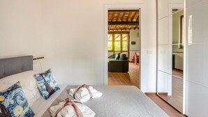 Een slaapkamer met een bed, kussens en handdoeken. Er is uitzicht op een zithoek met een bank en een eettafel.
